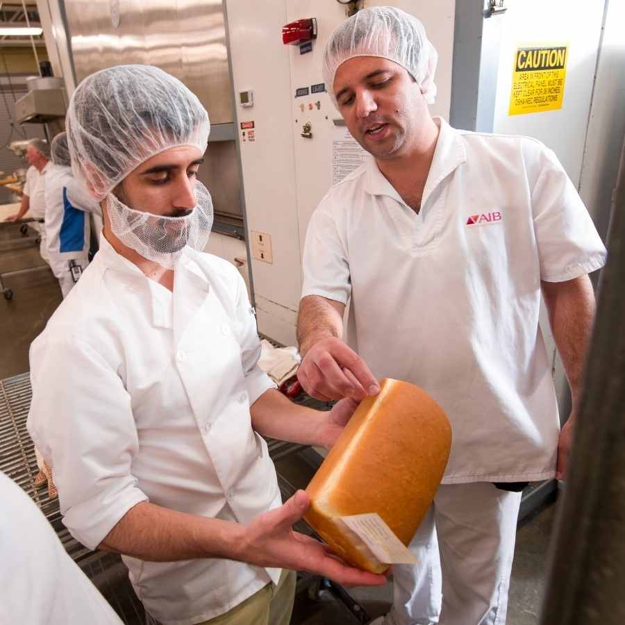 Two men inspecting a loaf of bread in a manufacturing facility