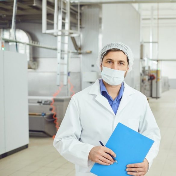 Man holding a clipboard wearing a hair net and face mask in a food processing facility