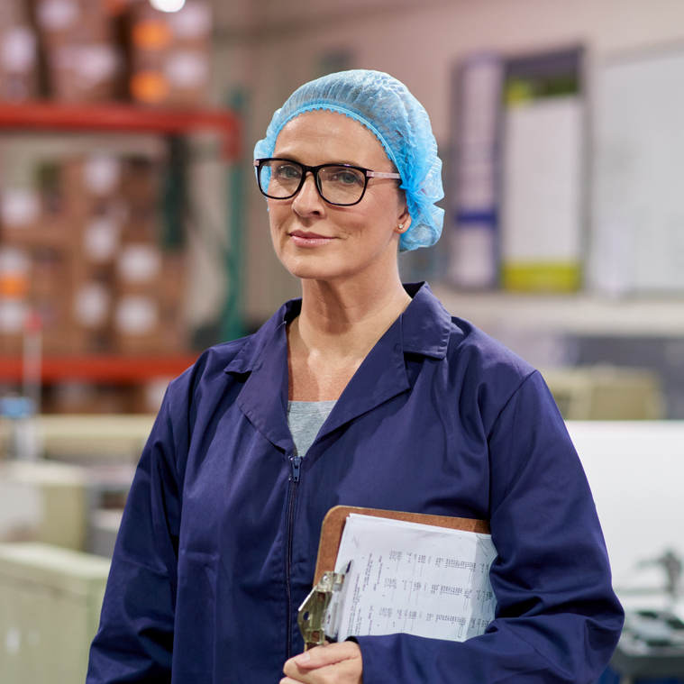 Woman wearing blue hairnet holding clipboard smiling at camera