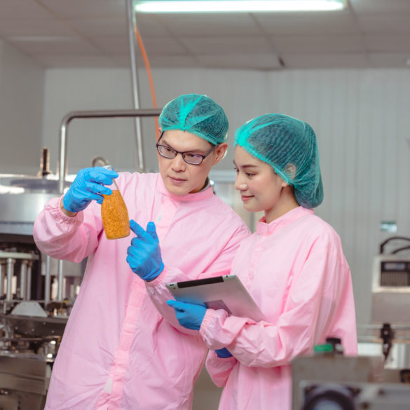 A man and a woman inspecting a bottle while wearing hair nets and gloves